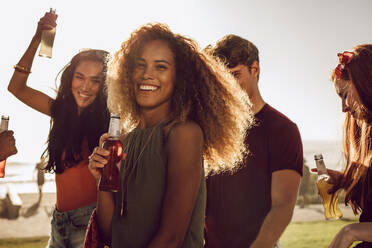 Fröhliche junge Frau mit Bier in der Hand, die mit ihren Freunden im Freien tanzt. Frau genießt Sommerferien mit Freunden. - JLPSF23531