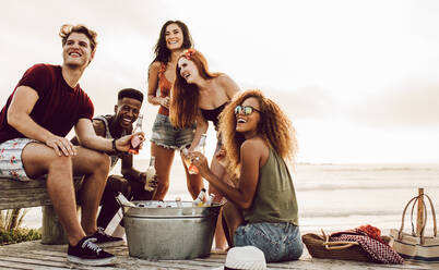 Junge Leute sitzen mit einem Bier am Strand und schauen sich etwas Interessantes an. Gemischtrassige Freunde hängen am Strand ab. - JLPSF23550