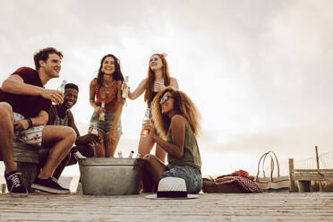 Group of men and women sitting at the beach with beers. Five young friends partying on the beach. - JLPSF23551