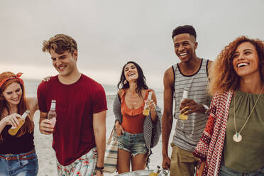 Group of people carrying beverage tub for party on beach. Diverse group of young people walking outdoors and having drinks. - JLPSF23560