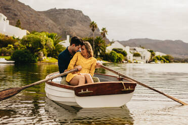 Young couple enjoying their boat date in a lake. Couple in love sitting together in a boat touching their heads looking at each other. - JLPSF23574