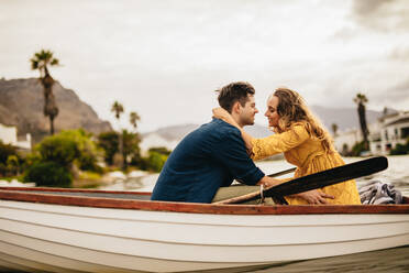 Seitenansicht eines Paares, das in einem Boot sitzt und sich unterhält. Verliebtes Paar auf einem Bootsausflug, das zusammensitzt und sich gegenseitig hält. - JLPSF23579