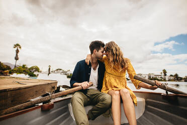 Young couple sitting in a boat touching their heads holding each other. Couple on a boat date in a lake sitting together holding the paddles. - JLPSF23585