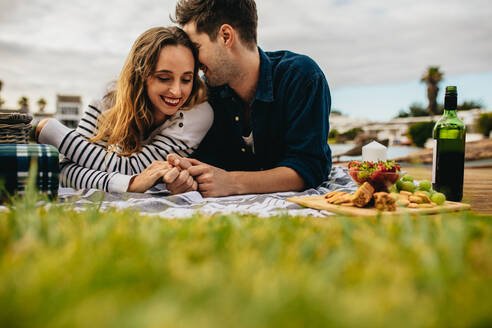 Verliebtes Paar bei einem Date, das Essen und Getränke im Freien genießt. Ein lächelnder Mann und eine lächelnde Frau liegen auf dem Boden, halten sich an den Händen und unterhalten sich bei einem Date. - JLPSF23596
