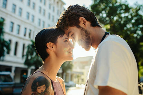Mann berührt Frau auf der Stirn mit seiner Stirn stehen auf der Straße mit Sonne im Hintergrund. Tourist Paar in einer glücklichen und romantischen Stimmung während der Erkundung der Stadt. - JLPSF23617