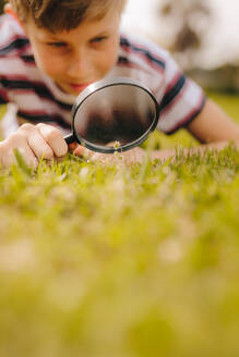 Kind spielt mit Lupe im Freien. Junge erkundet Garten mit Lupe im Park. - JLPSF23631