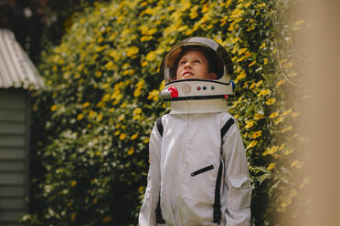 Junge, der so tut, als sei er ein Astronaut, der einen Raumanzug und einen Helm trägt, im Freien steht und nach oben schaut. Junge, der spielt, ein Astronaut zu sein. - JLPSF23641