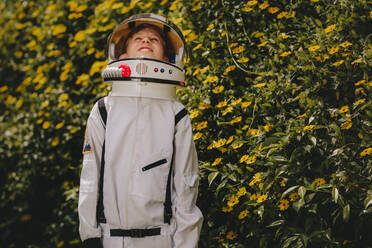 Boy wearing space suit and helmet standing outdoors and looking up. Cute boy in astronaut dress playing outdoors. - JLPSF23642