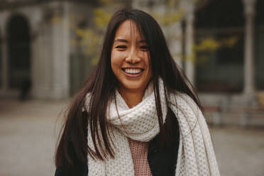 Nahaufnahme einer lächelnden Frau, die im Freien steht. Lächelnde asiatische Frau in Winterkleidung steht auf der Straße. - JLPSF23663