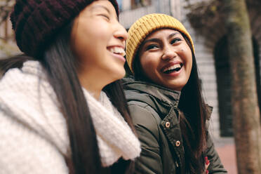 Seitenansicht von zwei asiatischen Frauen in Winterkleidung, die im Freien stehen. Frauen in warmer Kleidung lächeln und haben Spaß im Freien. - JLPSF23678