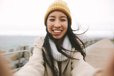 Fröhliche asiatische Frauen stehen an einem Wintermorgen mit offenen Armen im Freien. Lächelnde Frau in Winterkleidung steht an einem kalten Tag im Freien. - JLPSF23697
