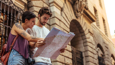 Touristenpaar, das mit Hilfe einer Karte den Weg zu seinem Ziel sucht. Ein Mann und eine Frau, die in der Nähe eines alten Steingebäudes stehen. - JLPSF23712