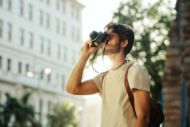 Ein Reisender fotografiert mit seiner Kamera und der Sonne im Hintergrund. Ein Tourist geht durch die Stadt und fotografiert. - JLPSF23718