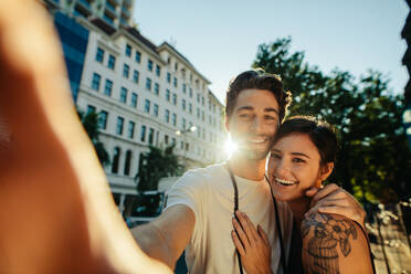 Glückliches Entdeckerpaar macht ein Selfie auf der Straße mit der Sonne im Hintergrund. Touristenpaar in glücklicher und romantischer Stimmung bei der Erkundung der Stadt. - JLPSF23723
