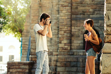 Ein Mann fotografiert seine Freundin mit einer Kamera. Ein Touristenpaar geht durch die Stadt und macht Fotos. - JLPSF23729