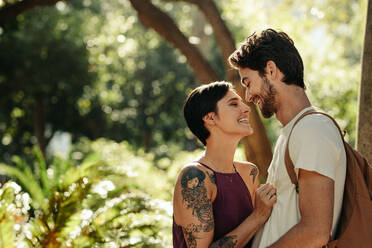 Eine Frau steht in der Nähe eines Mannes in einem Garten mit Bäumen im Hintergrund. Ein Touristenpaar in einer glücklichen und romantischen Stimmung erkundet die Stadt. - JLPSF23731