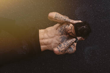 Fit young man doing abs crunches outdoors on a rainy day. Muscular man doing sit ups on a wet road. Top view shot. - JLPSF23753