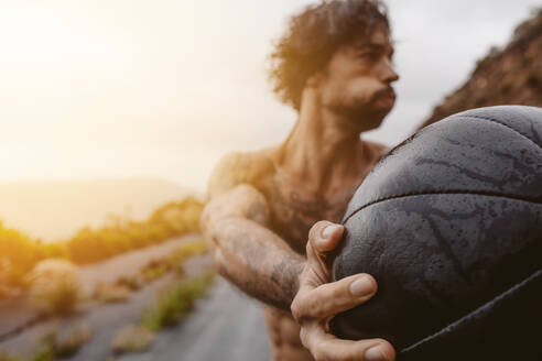 Hand eines jungen Mannes, der mit einem Medizinball im Freien trainiert. Sportler, der an einem regnerischen Tag im Freien trainiert. - JLPSF23755