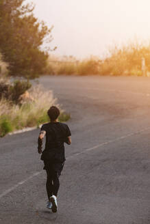 Gesunder Mann läuft auf einer Bergstraße. Rückansicht eines Sportlers, der auf einer Bergstraße für einen Marathon trainiert. - JLPSF23763