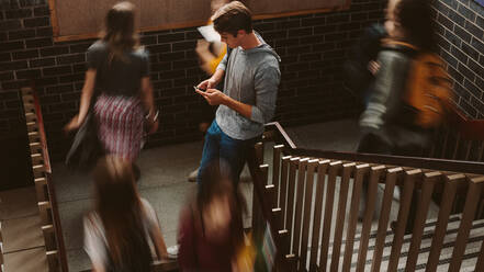 Junger Mann steht auf der Treppe in einem College mit vorbeilaufenden Mädchen. Studenten auf den Stufen eines College-Campus. - JLPSF23772