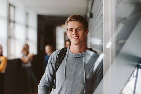 Porträt eines männlichen Studenten im Teenageralter, der im Korridor eines College steht. Kaukasischer männlicher Student auf dem Universitätscampus. - JLPSF23777