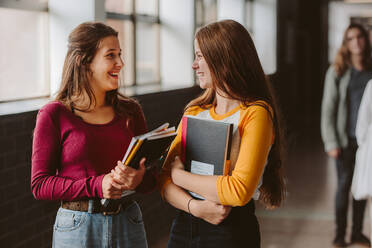 Zwei junge Frauen mit Buch, die sich auf dem Flur einer Hochschule unterhalten. Studenten auf dem Flur nach der Vorlesung. - JLPSF23778