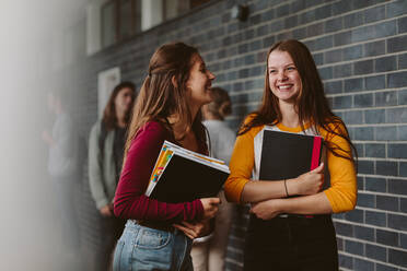 Portrait of smiling girls walking through high school corridor after their class. Two female college students after lecture. - JLPSF23779