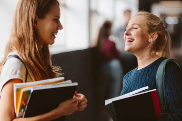 Zwei Studentinnen stehen nach dem Unterricht im Flur und unterhalten sich. Zwei Studentinnen unterhalten sich nach der Vorlesung und lachen. - JLPSF23782