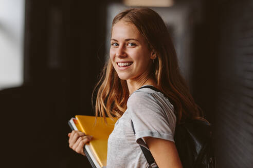 Rear view of beautiful girl walking through university hallway looking back and smiling. female student going for the lecture. - JLPSF23784