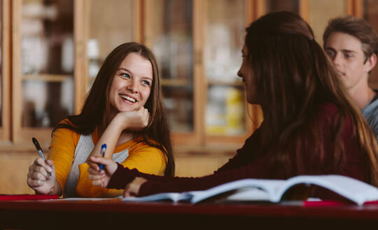 Lächelnde junge Frau, die im Klassenzimmer sitzt und sich mit Mitschülern unterhält. Universitätsstudenten im Klassenzimmer während einer Vorlesung. - JLPSF23790