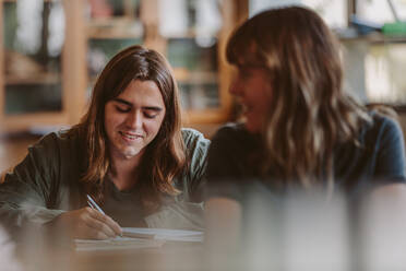 Junger männlicher Student, der während einer Vorlesung Notizen in ein Buch schreibt. Männlicher Student, der an der Universität studiert. - JLPSF23796