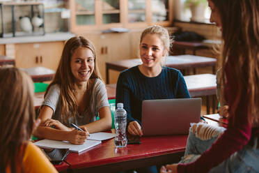 Eine Gruppe von Studenten unterhält sich nach der Vorlesung im Klassenzimmer. Studentinnen unterhalten sich in der Pause zwischen den Vorlesungen. - JLPSF23800