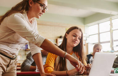 Lehrer hilft Studentin im Klassenzimmer, Dozentin zeigt auf Laptop-Bildschirm und zeigt einer Studentin etwas. - JLPSF23806