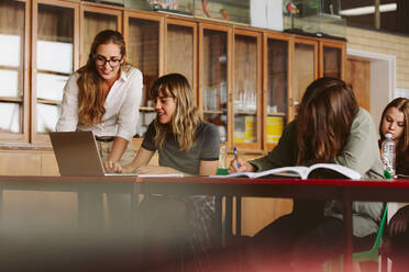 Happy young teacher helping a female student studying on laptop in classroom. Professor assisting students in lecture. - JLPSF23819