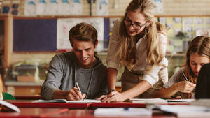 Porträt einer Lehrerin, die auf das Heft ihres Schülers blickt, während sie ihm Fehler erklärt. Die Lehrerin hilft dem Schüler während des Unterrichts. - JLPSF23821