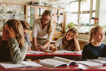 Gruppe von Universitätsstudenten, die eine Vorlesung auf dem Campus besuchen, mit einem Lehrer, der bei den Studien hilft. - JLPSF23823