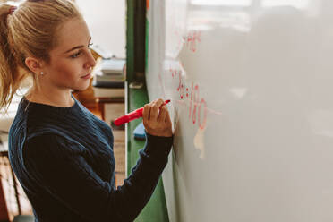 Nahaufnahme einer Schülerin, die eine Gleichung auf eine Tafel im Klassenzimmer schreibt. Ein Mädchen schreibt während des Matheunterrichts auf eine Tafel. - JLPSF23828