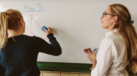 Rückansicht eines jungen Schülers, der an der Tafel schreibt, während der Lehrer im Klassenzimmer steht. Ein Schüler schreibt während des Geometrieunterrichts an der Tafel. - JLPSF23829