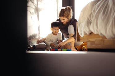 Mutter und Sohn spielen mit Spielzeug im Schlafzimmer. Junge Frau spielt mit ihrem Sohn Blockspiele. - JLPSF23842