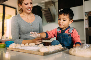 Kleiner Junge hat Spaß beim Kekse backen mit seiner Mutter in der Küche. Frau sieht ihren Sohn an, der Spaß hat, während er einen Teig für Kekse macht. - JLPSF23860