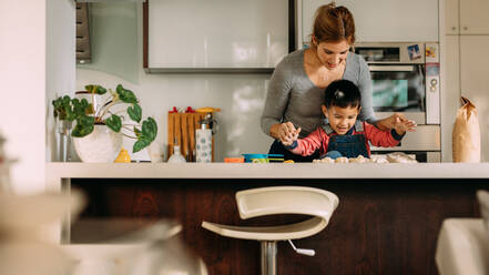 Glückliche junge Mutter und Sohn beim Kekse backen mit Teig in der Küche. Kleiner Junge hat Spaß beim Kekse backen mit Mutter mit Teig zu Hause. - JLPSF23862