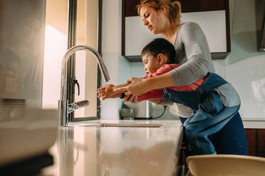 Niedlicher Sohn wäscht sich nach dem Kochen die Hände mit seiner Mutter im Waschbecken. Frau hilft kleinem Jungen beim Händewaschen am Waschbecken. - JLPSF23865