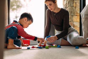 Mutter und Sohn spielen mit buntem Spielzeug zu Hause. Junge Frau verbringt ihre Freizeit mit ihrem Sohn. Mutter und Kind spielen mit Holzklötzen. - JLPSF23867
