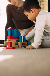 Cute Kind spielt mit bunten Holzklötzen mit seiner Mutter sitzt durch. Kind spielt mit bunten Spielsachen mit Mutter zu Hause. - JLPSF23869