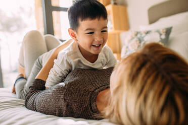 Cute little kid playing with his mother on bed. Mother and son having a fun time at home. - JLPSF23870