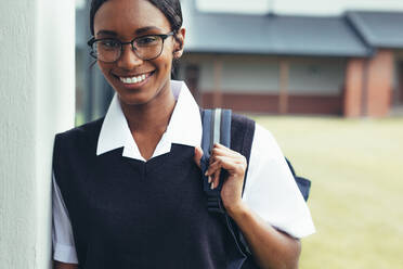 Teenager-Mädchen mit Schultasche, das durch den Korridor der High School geht. Weibliche Schülerin in Uniform schaut in die Kamera und lächelt. - JLPSF23880