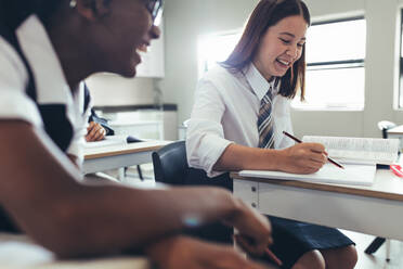 Female students in classroom smiling while studying. High school girls making notes and smiling in class. - JLPSF23892