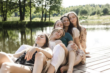 Lächelnde junge Freunde mit geschlossenen Augen, die sich am Pier aneinander lehnen - LLUF00909