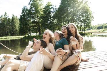 Glückliche junge Freunde, die sich am Pier aneinander lehnen - LLUF00910