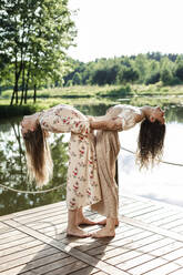 Young friends bending over backwards by holding each other on pier - LLUF00954